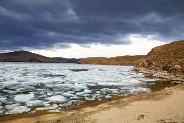 Spring landscape of Lake Baikal on a cloudy day. Ice drift, large ice floes floating in the lake....