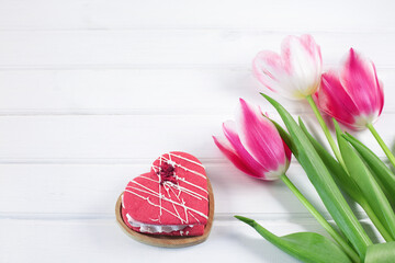 Colorful tulips and hearts cookie on white wooden background.