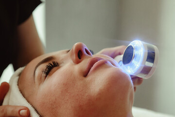 Beautician doing led light therapy to woman with problematic skin in SPA