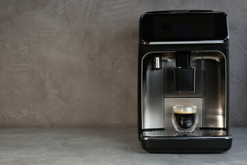 Modern espresso machine with glass of coffee on grey table, space for text