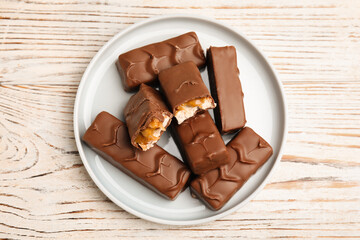 Plate of chocolate bars with caramel, nuts and nougat on white wooden table, top view