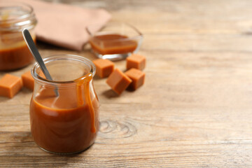 Tasty salted caramel and spoon in glass jar on wooden table, space for text