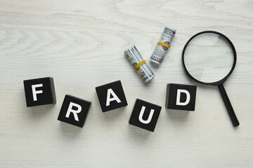 Black cubes with word Fraud, money and magnifying glass on white wooden table, flat lay