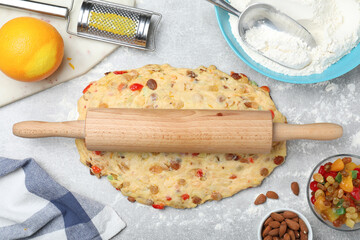 Raw dough for Stollen with rolling pin surrounded by ingredients at grey table, flat lay. Baking traditional German Christmas bread