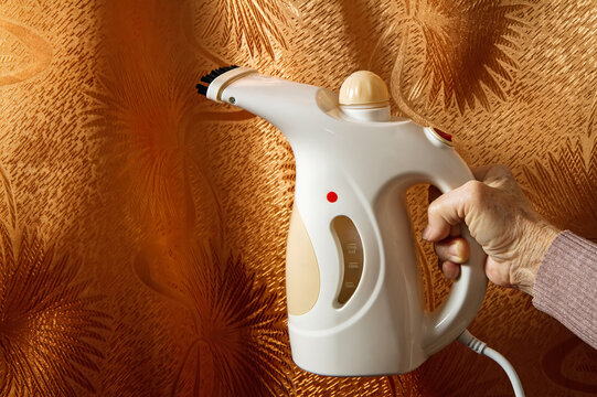 A steam iron in the hand of an elderly woman.