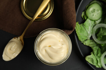 Obraz na płótnie Canvas Jar and spoon with delicious mayonnaise near fresh salad on black table, flat lay