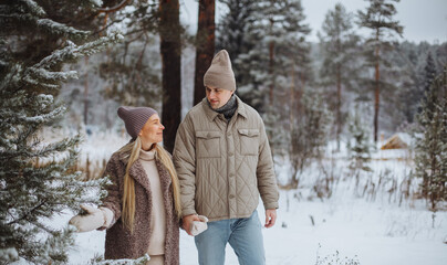 A young couple in love walks through the winter snowy forest. A man with a smile looks at his girlfriend