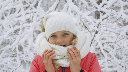 A beautiful young girl in a white winter hat. She looks into the camera smiling sincerely,...