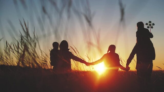 people in the park. happy family walk silhouette at sunset light. mom, dad and daughters walk holding a hands in park. concept of happy family childhood dream. parents and kids come back silhouette