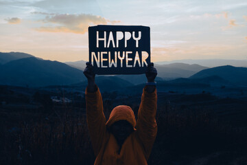 Hands hold HAPPY NEW YEAR design from cardboard against the background of mountain with sunset. Happy New Year concept.