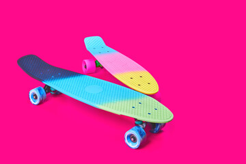 Two neon rainbow colored Penny board skateboards isolated on solid bright crimson background. Plastic mini cruiser. Youth minimalistic Sport inspired summer fun concept. Copy space.