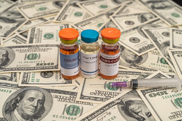 vaccine bottles during a pandemic with a calculator with a large sum of dollar bills.