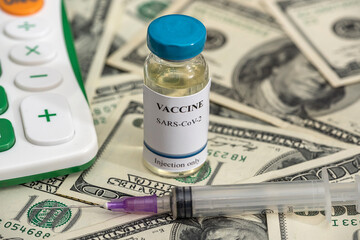 vaccine bottles during a pandemic with a calculator with a large sum of dollar bills.