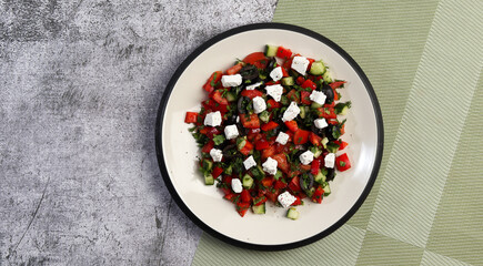 Fototapeta na wymiar Greek salad with cucumbers, tomatoes, onions, olives, feta cheese and herbs on a round plate on a dark gray background. Top view, flat lay