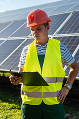 Worker in helmet in protective vest posing against solar panels station