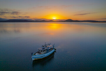 Naklejka premium Sunrise waterscape with a boat, soft clouds and golden glow