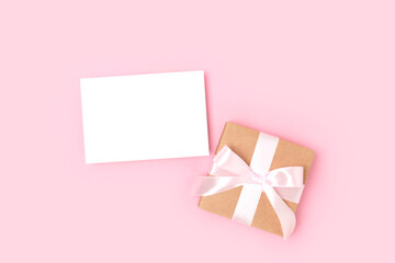Blank paper sheet mockup and present tied with a ribbon on a pink pastel background. Gift box and greeting card template.
