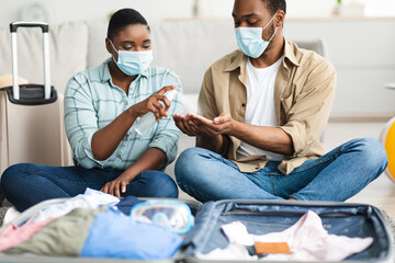 Fototapeta premium Black Couple Wearing Face Masks Spraying Sanitizer On Hands Indoor