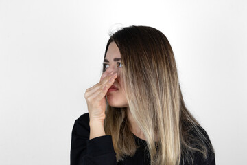 Displeased woman covers nose with hand, smells something awful, pinches nose, frowns in...