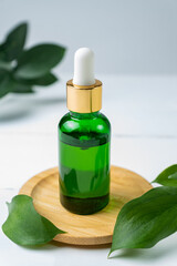 Green glass cosmetic bottle with a dropper on a white background with tropical leaves. Natural cosmetics concept, natural essential oil and skin care products