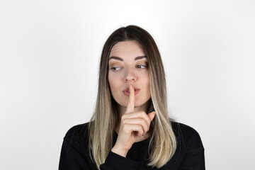 Girl showing Silence gesture on white background. Top secret! Do not say to anyone! Asking to be quiet with finger on lips pointing with hand to the side. silence and secret concept. She looks left.