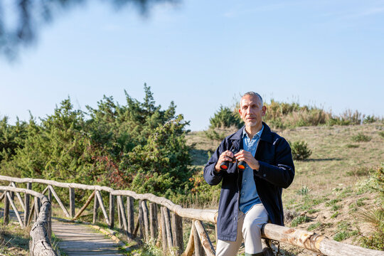 Man with binoculars sitting on railing at wooden bridge