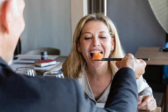 Man feeding sushi to woman through chopsticks on lunch date at restaurant