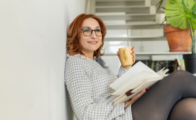 Contemplative woman with diary and mug sitting on stairs at home