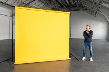 Thoughtful businessman looking at blank yellow backdrop in industial hall
