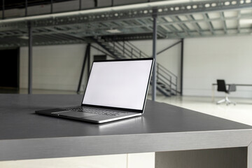 Laptop with blank screen at desk in industial hall