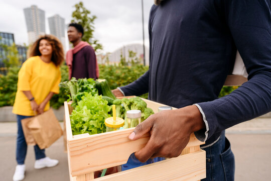 Man carrying basket of vegetables and friends in background on street