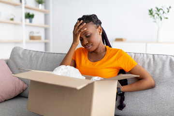 Disappointed black woman unboxing her delivery, looking inside wrong box, touching her forehead in...