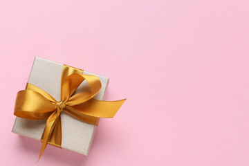 Gift box with golden bow on pink background, top view. Space for text