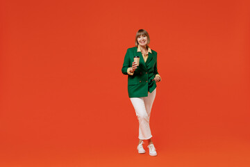 Full body elderly woman 50s in green classic suit hold takeaway delivery craft paper brown cup coffee to go isolated on plain orange color background studio portrait People business lifestyle concept