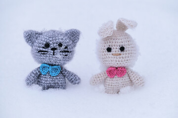 Easter bunny. Christmas gift knitted handmade animal dolls. White amigurumi rabbit with pink bow tie and gray kitten with blue tie. Toys hare and cat on white snow.