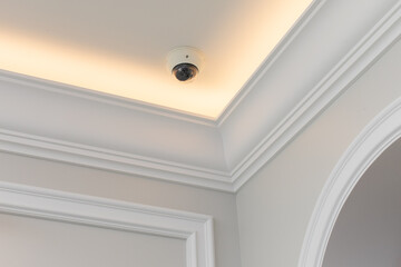 Dome surveillance video camera mounted on the ceiling of the classic design room with moldings and ceiling skirting