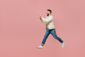 Fototapeta na wymiar Full body side view young happy man 20s wearing trendy jacket shirt hold in hand use mobile cell phone jump high walk go isolated on plain pastel light pink background studio People lifestyle concept