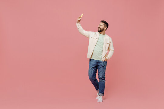Full body young smiling fun man 20s in trendy jacket shirt doing selfie shot on mobile cell phone post photo on social network isolated on plain pastel light pink background People lifestyle concept