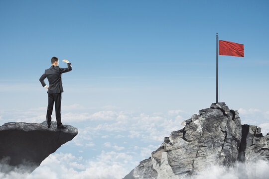 Abstract image of businessman looking into the distance while standing on edge of cliff, mock up place on sky with clouds background, red flag. Success, challenge, future and growth concept.