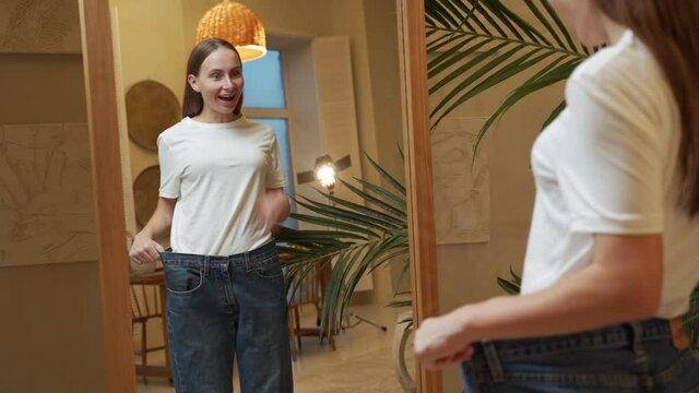 A woman who has lost a lot of weight due to a diet looks in the mirror and shows big jeans