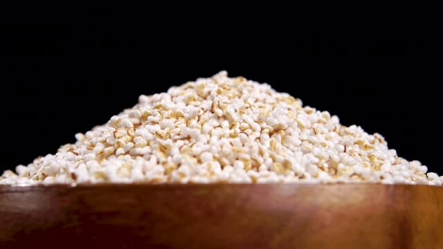Puffed amaranth seeds in wooden bowl. Popped amaranthus grain on a black background. Macro. Turning