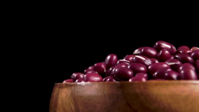 Full wooden bowl of red adzuki beans on black background. Macro. Rotation. Vigna angularis grains