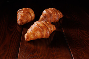 Several croissants lie on a dark varnished table.