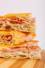 Tre pezzi di focaccia croccante ripiena di mortadella fresca sovrapposti a formare una piccola torre e poggiati su un tagliere di legno
