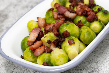 Brussels sprouts with bacon lardons in a traditional enamel dish.  On a concrete background