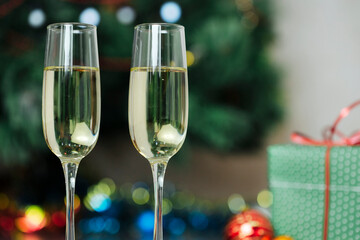 Champagne glasses and gifts, with New Year's toys near the Christmas tree decorated with colorful lights and a garland. close-up