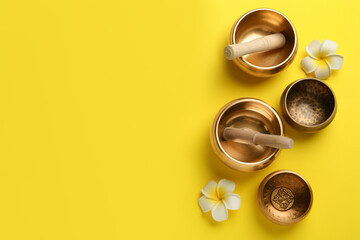 Golden singing bowls, mallets and flowers on yellow background, flat lay. Space for text