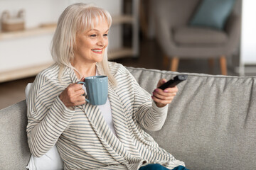 Smiling mature woman watching tv holding remote control