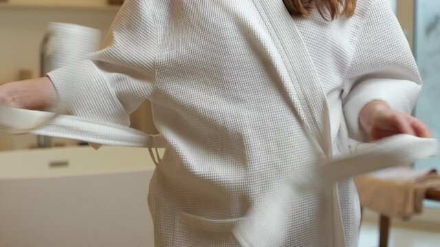 Slender young woman taking off her robe to take a relaxing bubble bath
