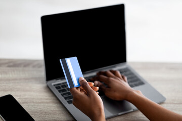 Distance shopping concept. Cropped view of black woman with credit card and laptop purchasing on...